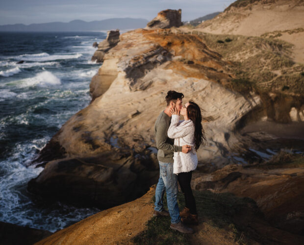 engaged couple kisses on a cliffside with epic views of the oregon coastline 1