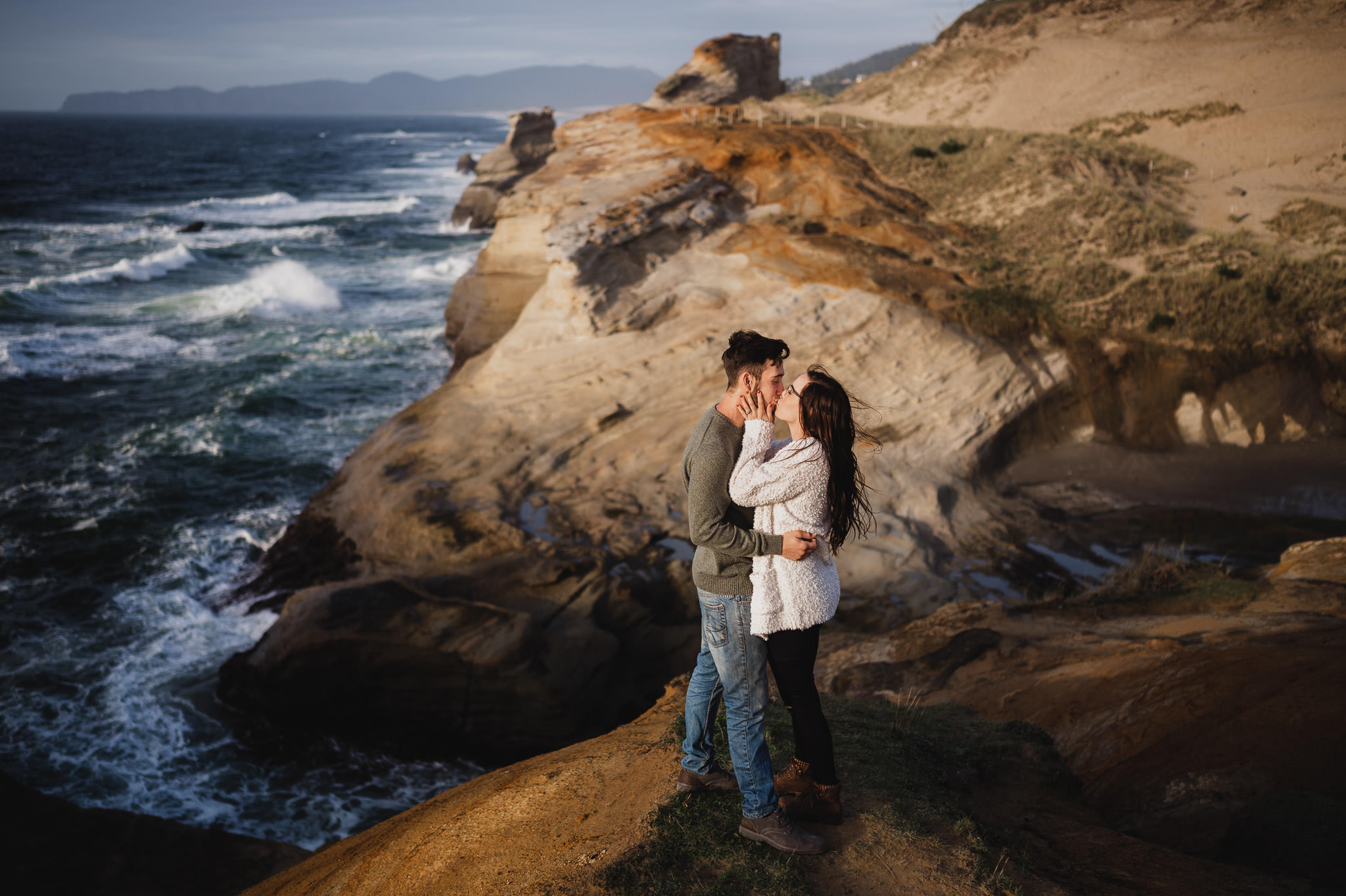 engaged couple kisses on a cliffside with epic views of the oregon coastline 1