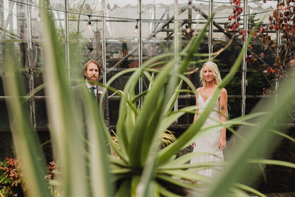 A wedding portraits of newlyweds standing next to each other by a greenhouse at Pomarius Nursery during their wedding at Castaway Portland, a wedding venue with an industrial vibe.
