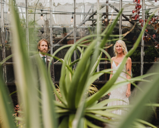 A wedding portraits of newlyweds standing next to each other by a greenhouse at Pomarius Nursery during their wedding at Castaway Portland, a wedding venue with an industrial vibe.
