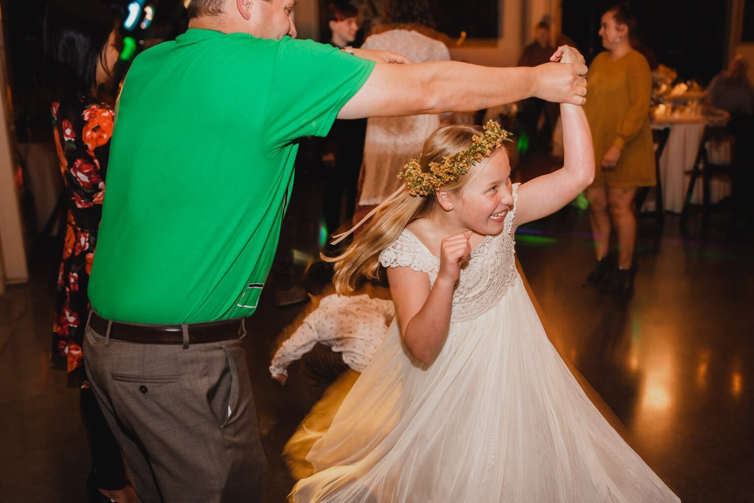 At a lively indoor event, a girl in a white dress dances happily with a man in a green shirt. It looks like they could be part of wedding photos at Castaway Portland.
