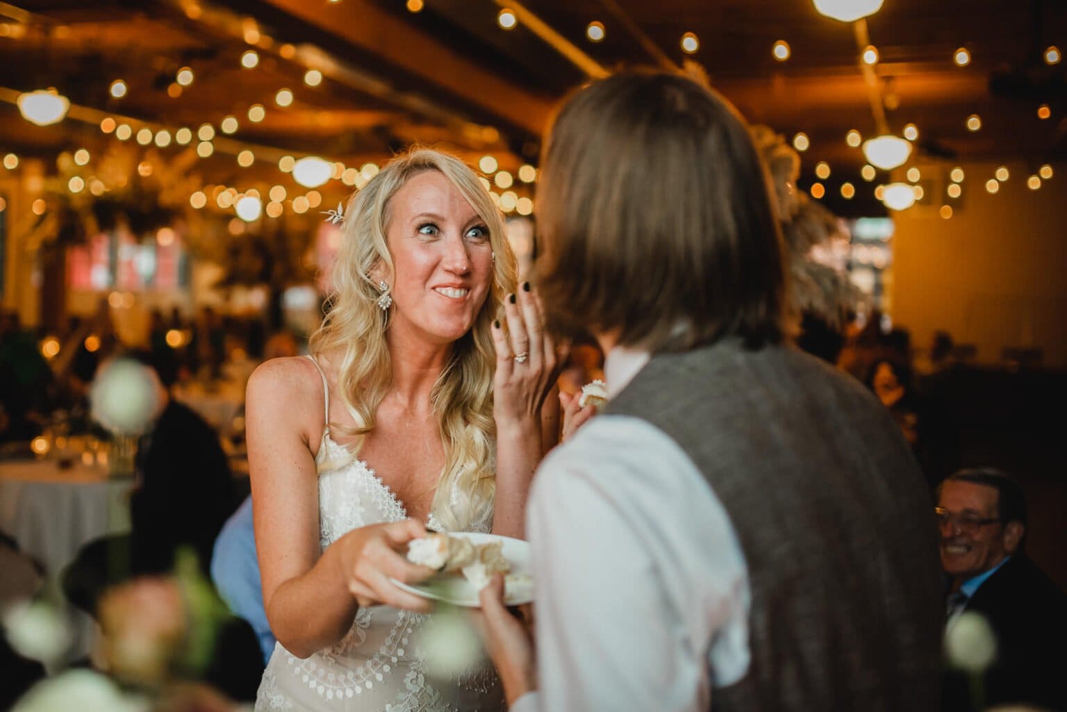 Bride and groom smiling and feeding each other cake at a warmly lit wedding reception, capturing the joy of their special day with stunning wedding photos at Castaway Portland.