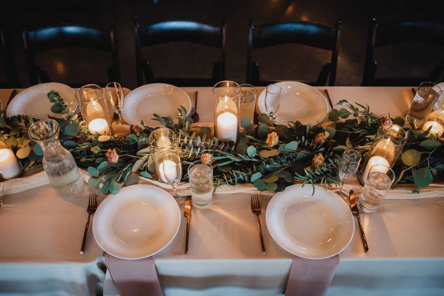 An elegant table setting with plates, glasses, and candles arranged on a floral centerpiece. The soft lighting creates a warm ambiance, perfect for capturing stunning wedding photos at Castaway Portland.