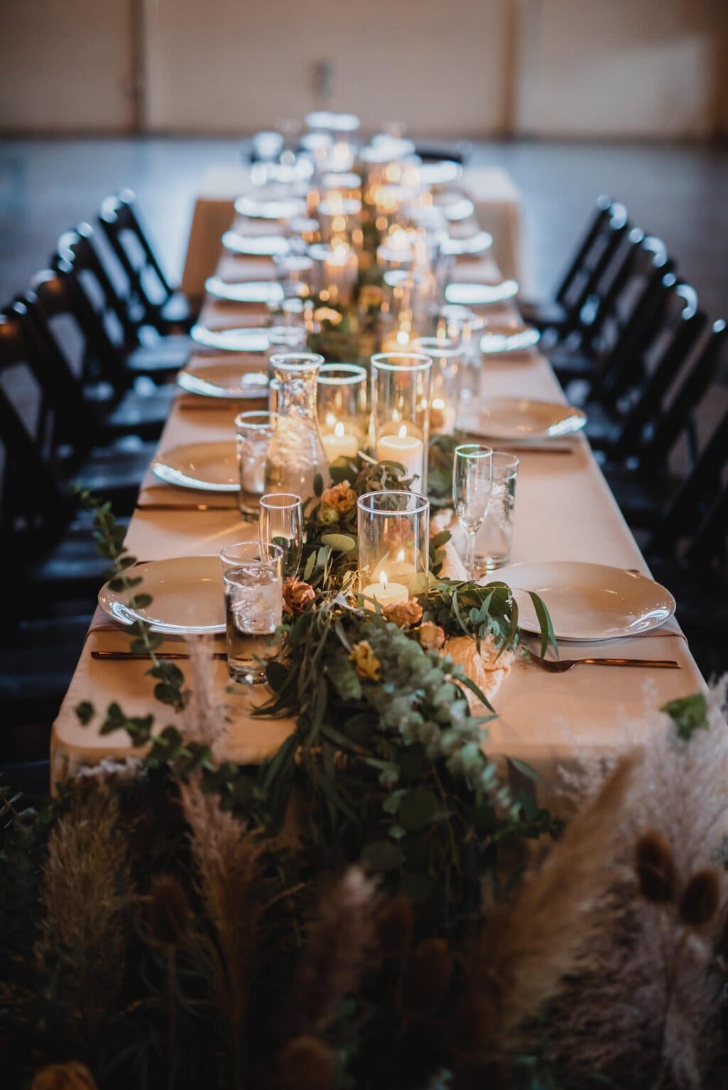 An elegant table setting features candles, plates, and a lush green floral centerpiece on a long wooden table, perfect for capturing stunning wedding photos at Castaway Portland.