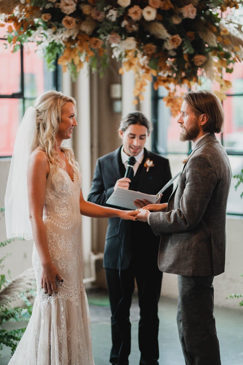 The bride and groom exchange vows with an officiant in a venue decorated with flowers, capturing the moment perfectly for their wedding photos at Castaway Portland.