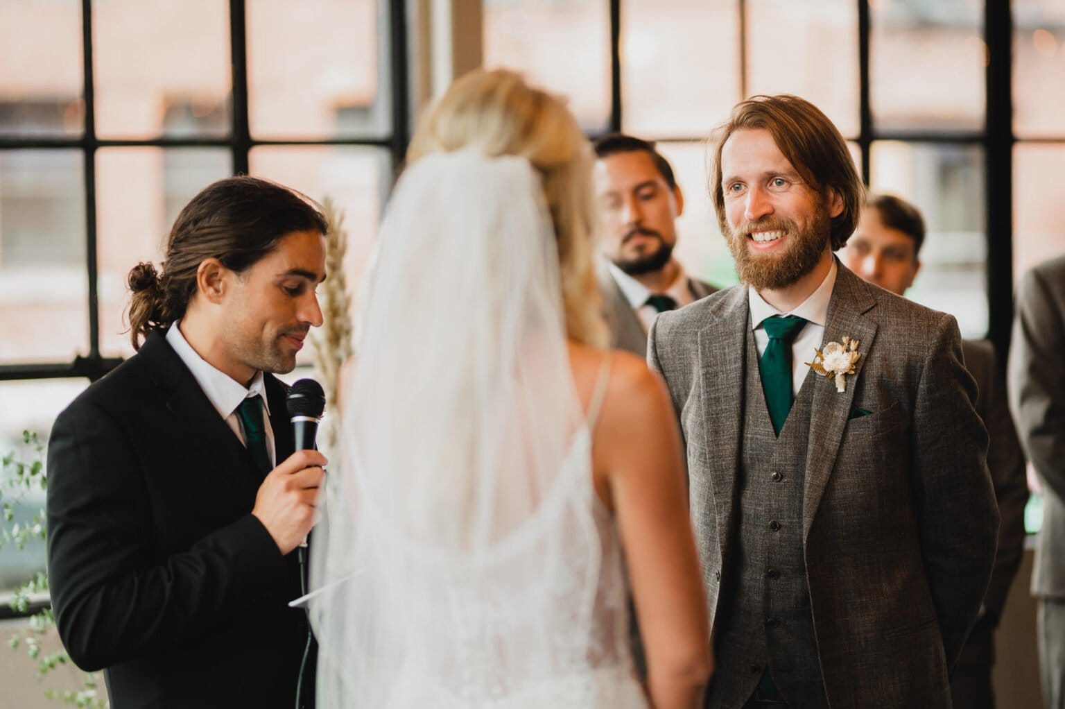 The bride and groom smile radiantly during their wedding ceremony as the officiant holds a microphone, capturing perfect wedding photos at Castaway Portland.