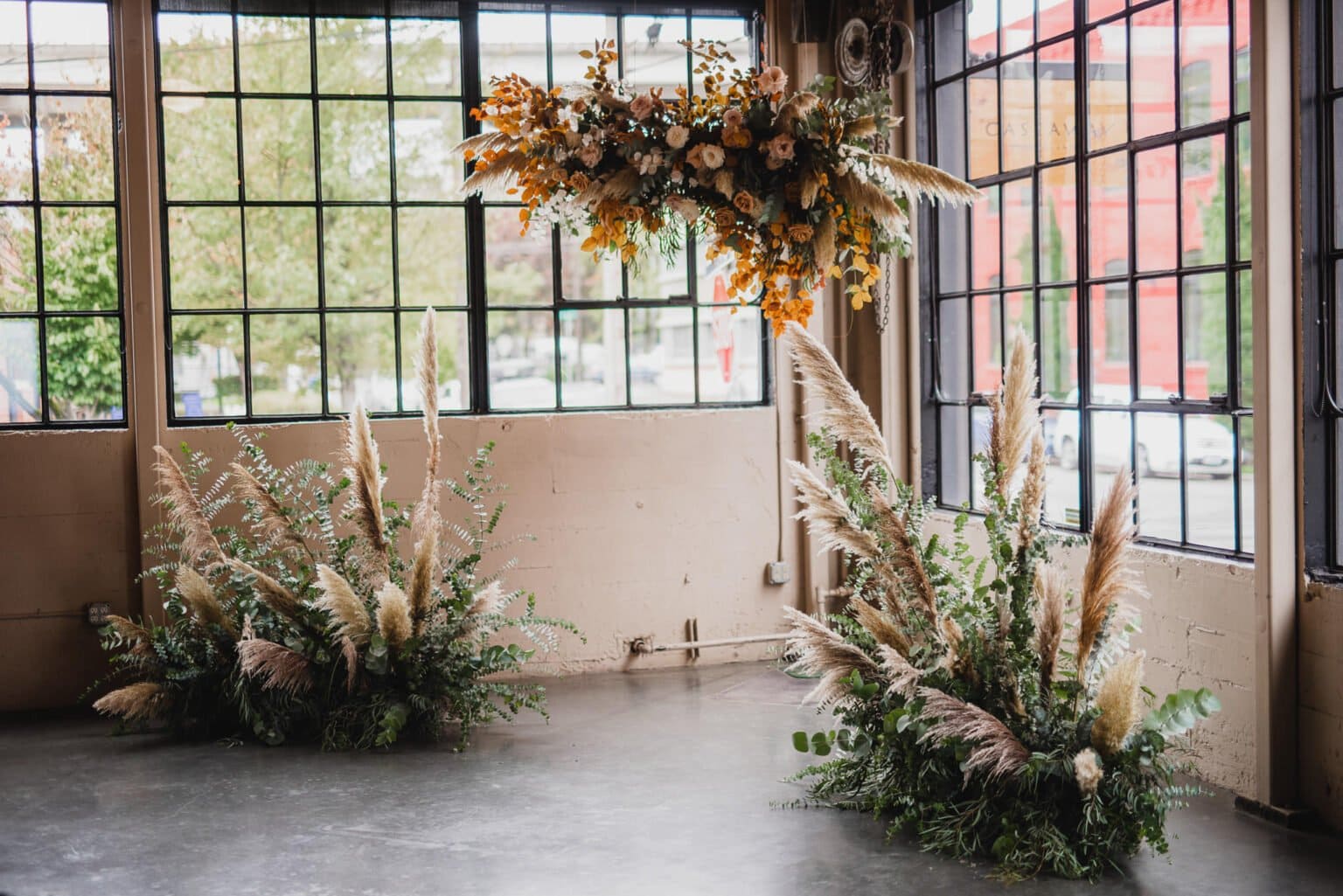 Indoor space perfect for wedding photos at Castaway Portland, featuring pampas grass arrangements and a hanging floral display near large windows.