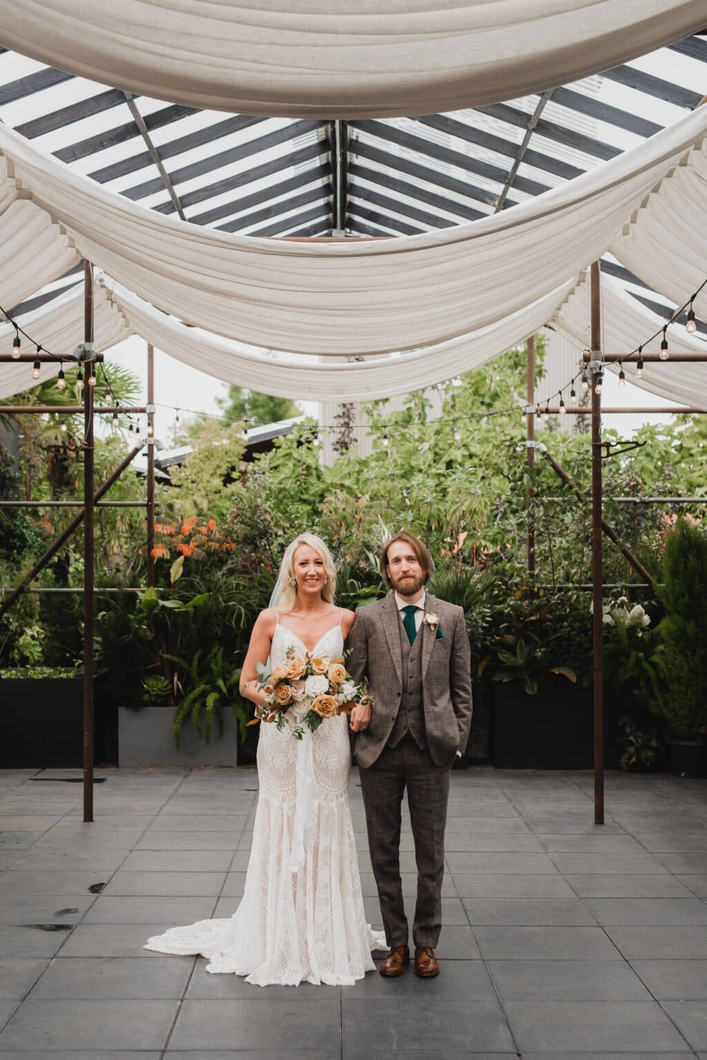 A couple in wedding attire poses under a canopy surrounded by greenery, capturing stunning portraits at Blockhouse before their wedding at Castaway Portland.