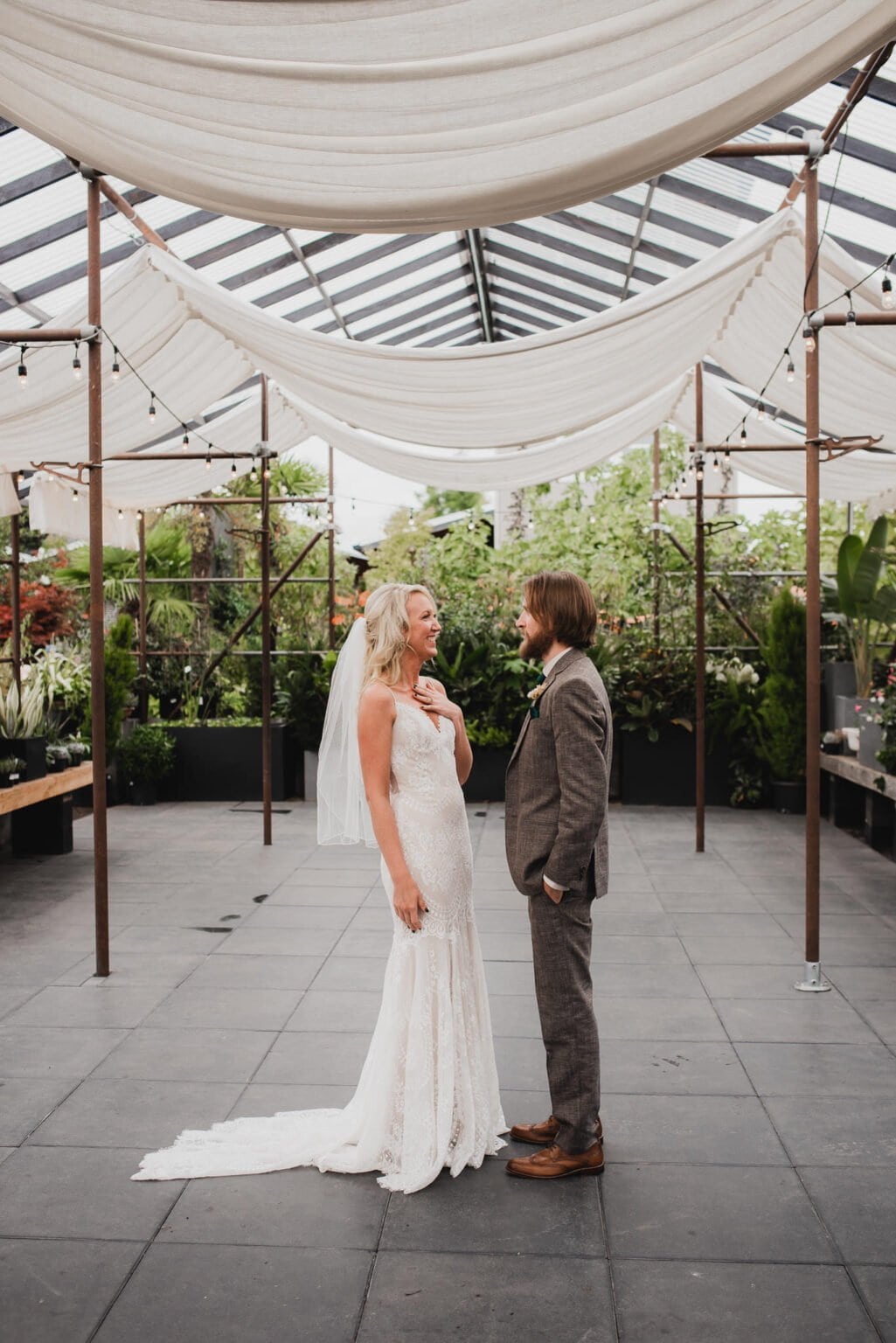 The bride and groom stand under a garden canopy, facing each other, capturing a serene moment before heading to portraits at Blockhouse ahead of their wedding at Castaway Portland.