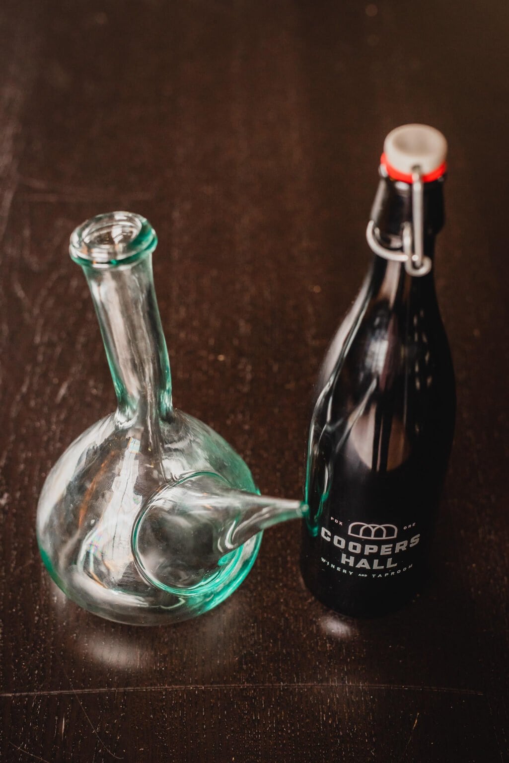A glass decanter sits next to a sealed Coopers Hall bottle on a dark wooden surface, setting a sophisticated scene perfect for capturing wedding photos at Castaway Portland.