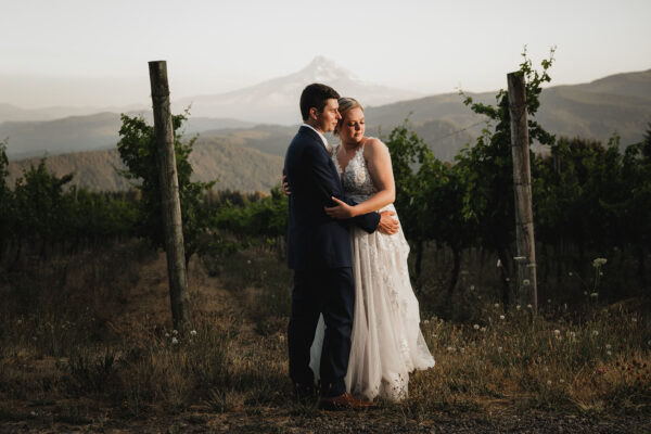 Newlyweds embrace during sunset at Gorge Crest Vineyards with Mt Hood in the background.