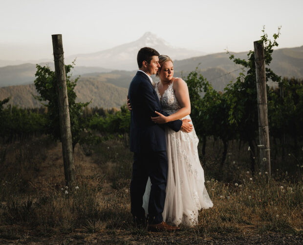 Newlyweds embrace during sunset at Gorge Crest Vineyards with Mt Hood in the background.