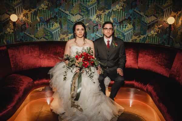 A wedding portrait of newlyweds sitting stoically on a sofa at Voysey, a speakeasy under their wedding venue, The Evergreen, in Portland, Oregon.