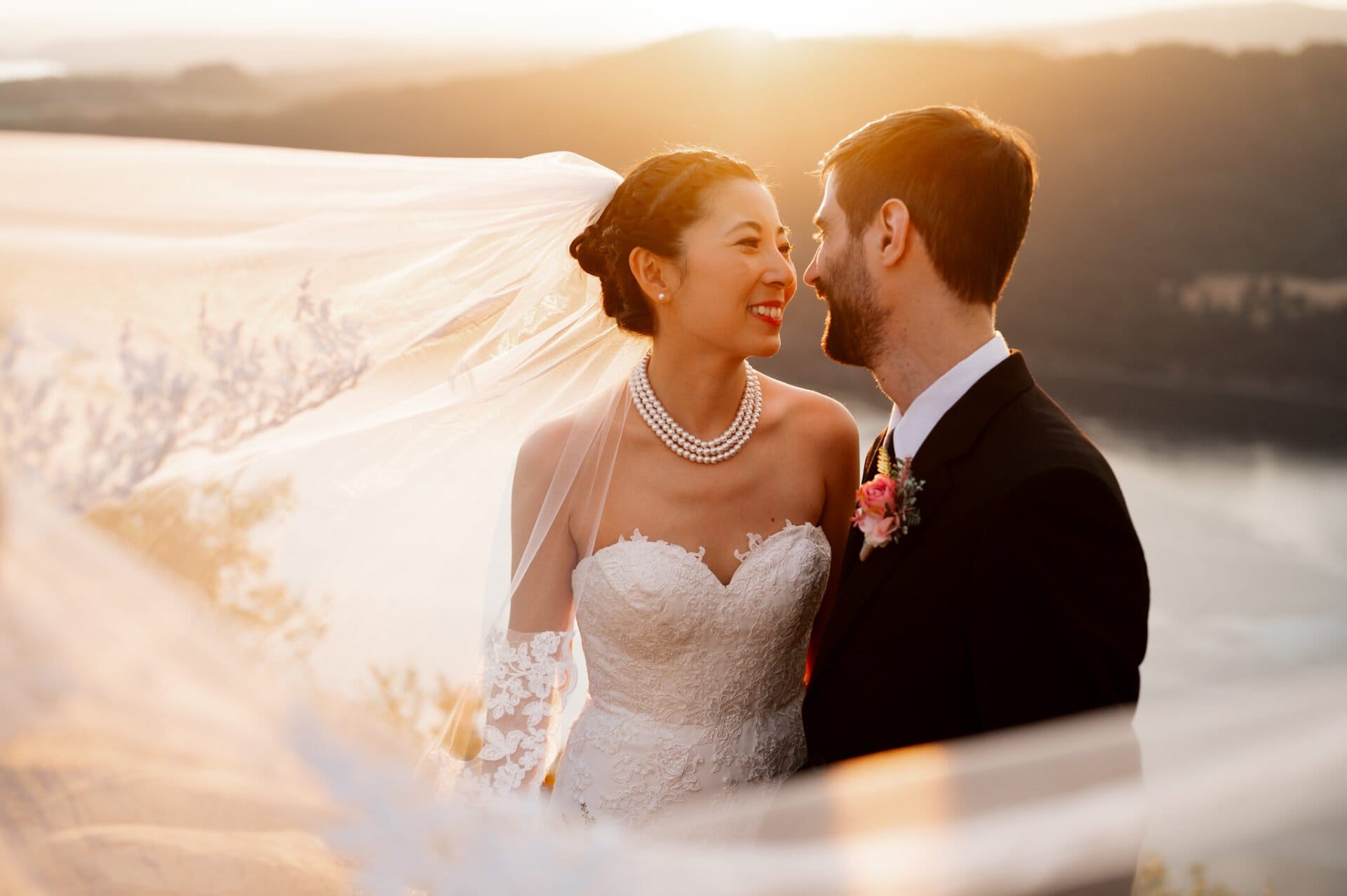 During her Angel's Rest elopement, a bride and groom embrace at sunset while the bride's veil blows around them in the wind.