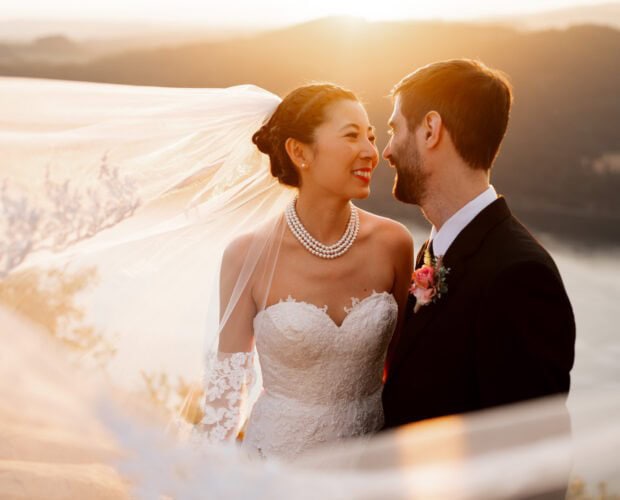 During her Angel's Rest elopement, a bride and groom embrace at sunset while the bride's veil blows around them in the wind.