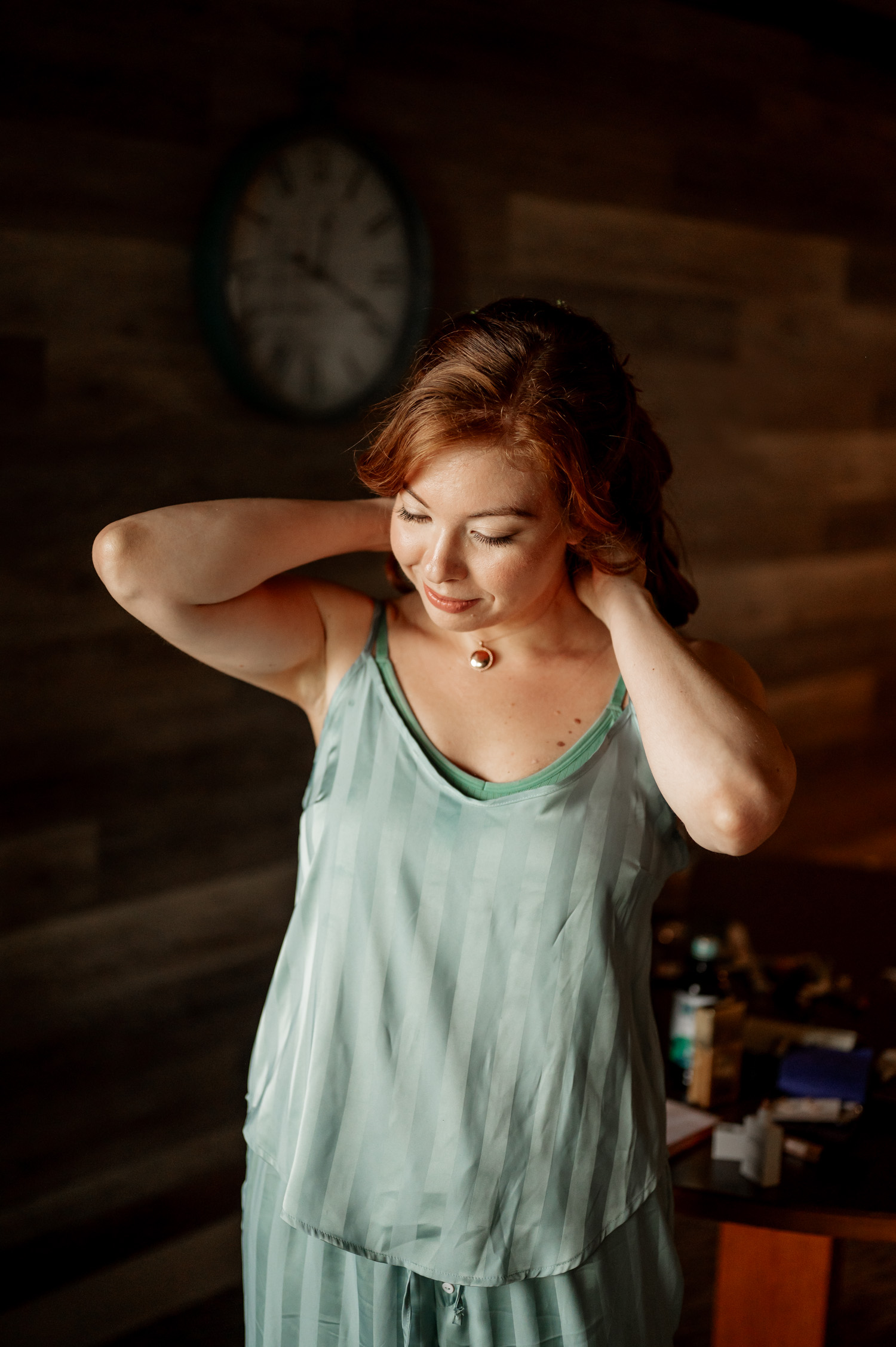 A woman in a green dress smiles while adjusting her hair at the Overleaf Lodge and Spa. A blurred clock is visible in the background.