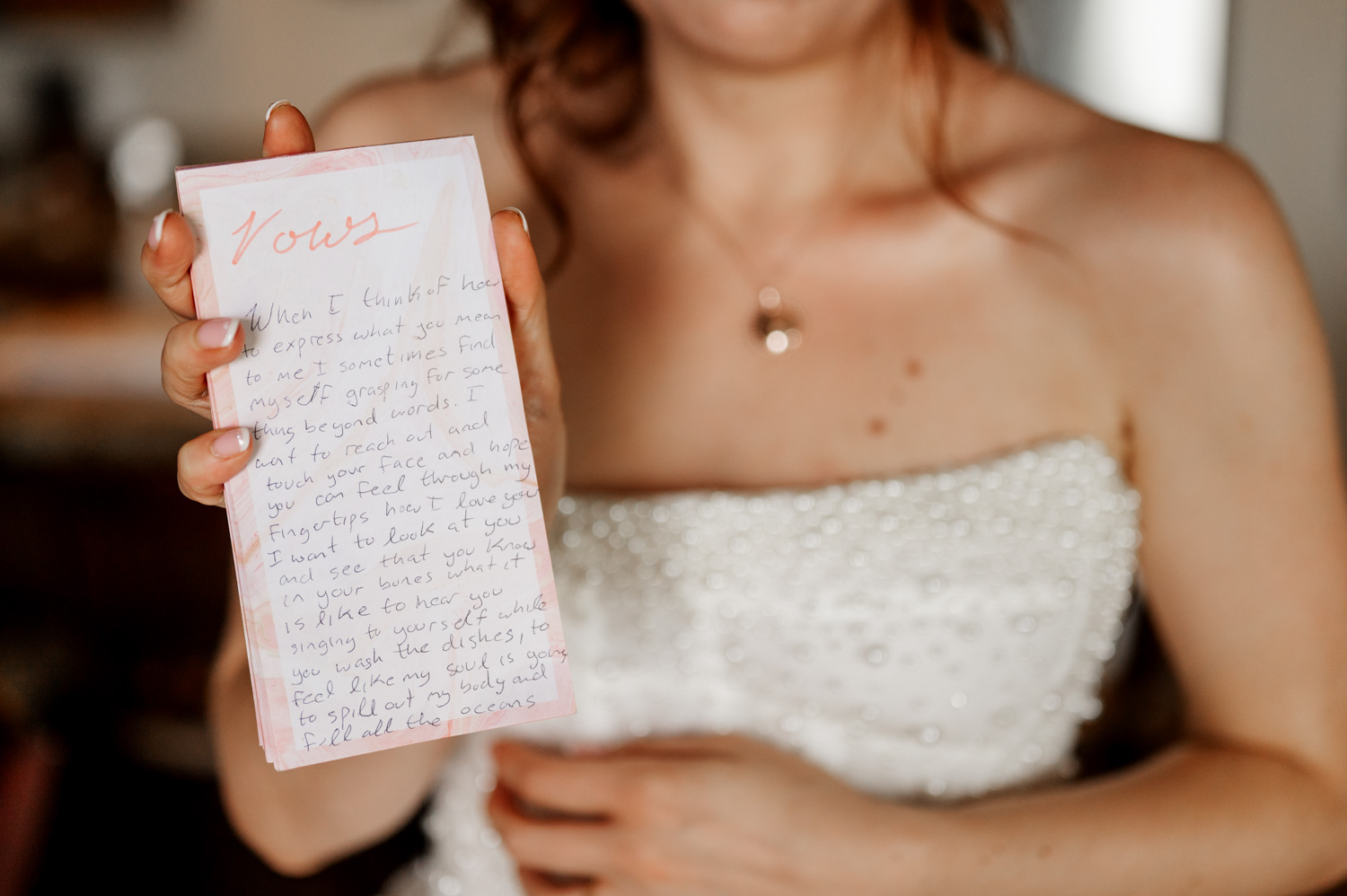 Bride with red hair in a white beaded gown holds handwritten vows while getting ready at Overleaf Lodge and Spa before her wedding at The Yachats Inn.