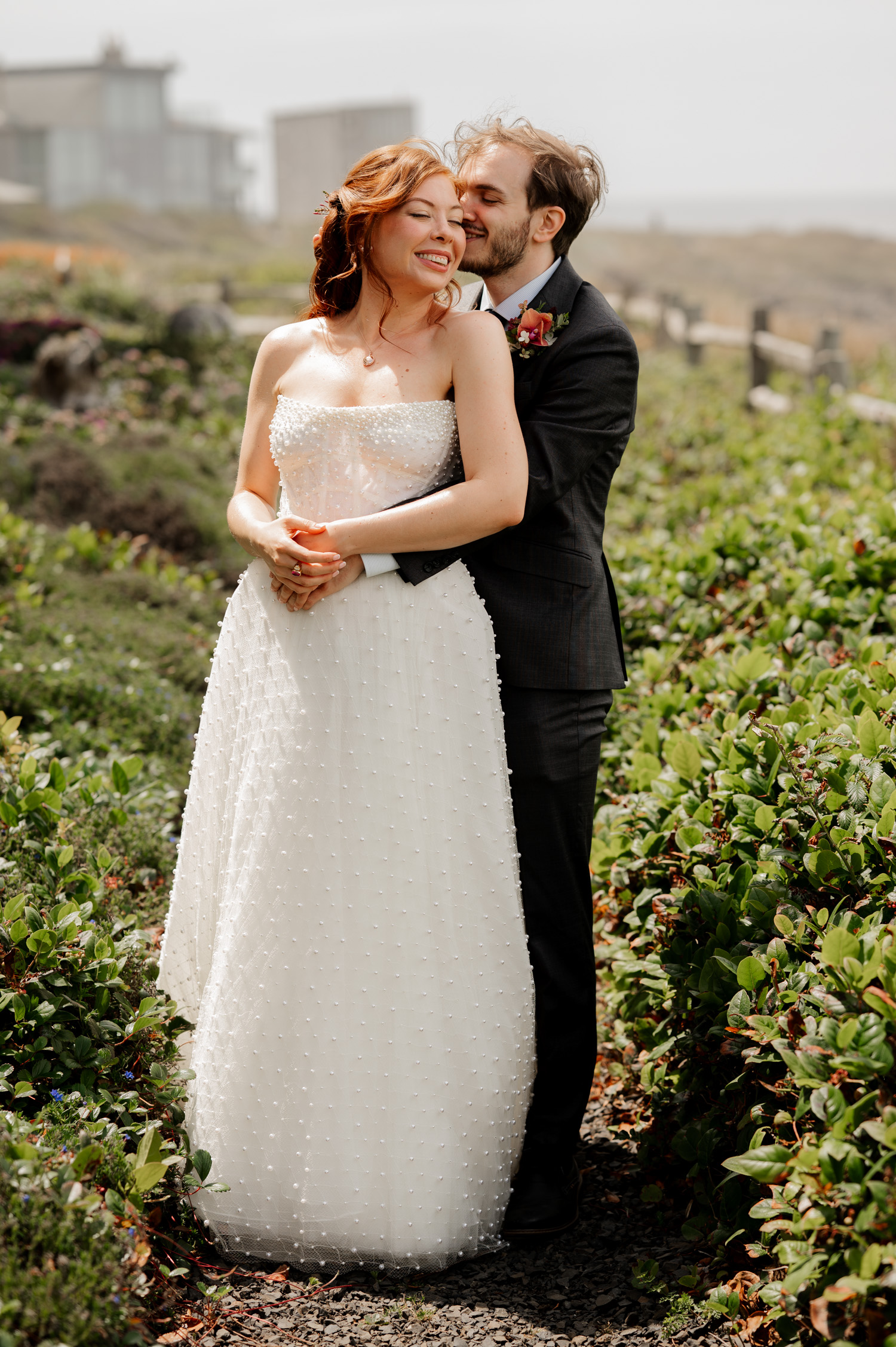 Bride and groom smiling and embracing on a path surrounded by lush greenery at the Overleaf Lodge and Spa.