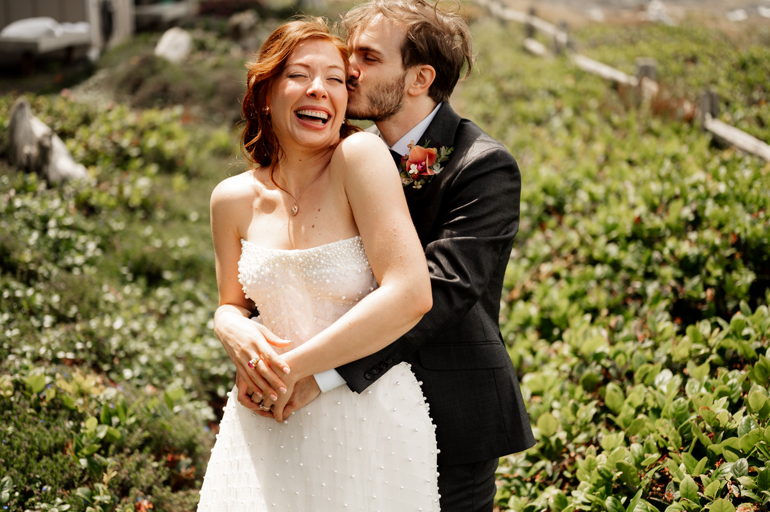 The bride and groom laugh and embrace in a lush green outdoor setting, capturing wedding portraits at the Overleaf Lodge and Spa before heading to their ceremony.