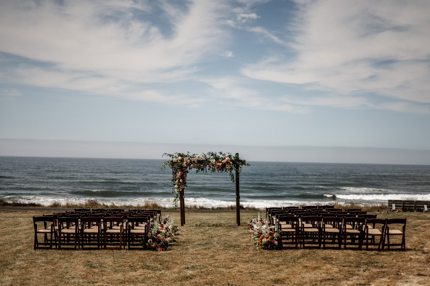 Outdoor wedding setup by the ocean at Yachats Inn, featuring an arch decorated with florals and rows of chairs on a grassy area.