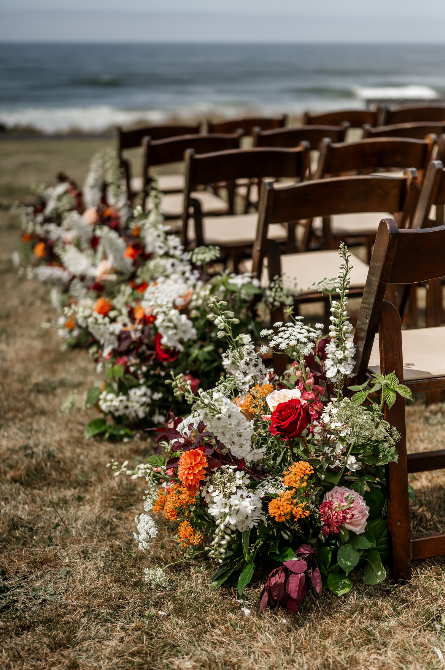 Outdoor wedding setup with rows of wooden chairs and vibrant floral arrangements, positioned to overlook the ocean at the Yachats Inn.