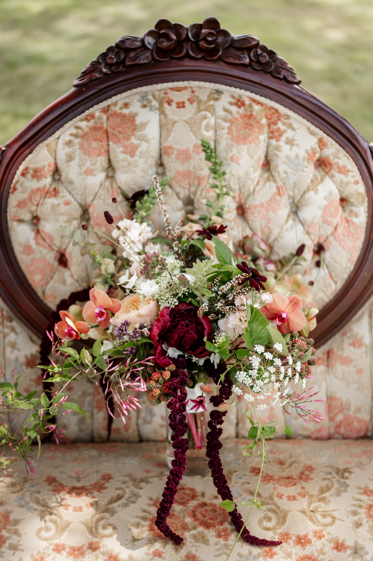 A bouquet of flowers with greenery placed on a vintage floral-patterned chair with wooden carvings.