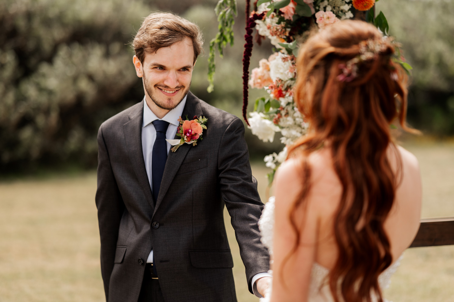Groom smiling at bride during an outdoor ceremony with colorful flowers in the background at the Yachats Inn.