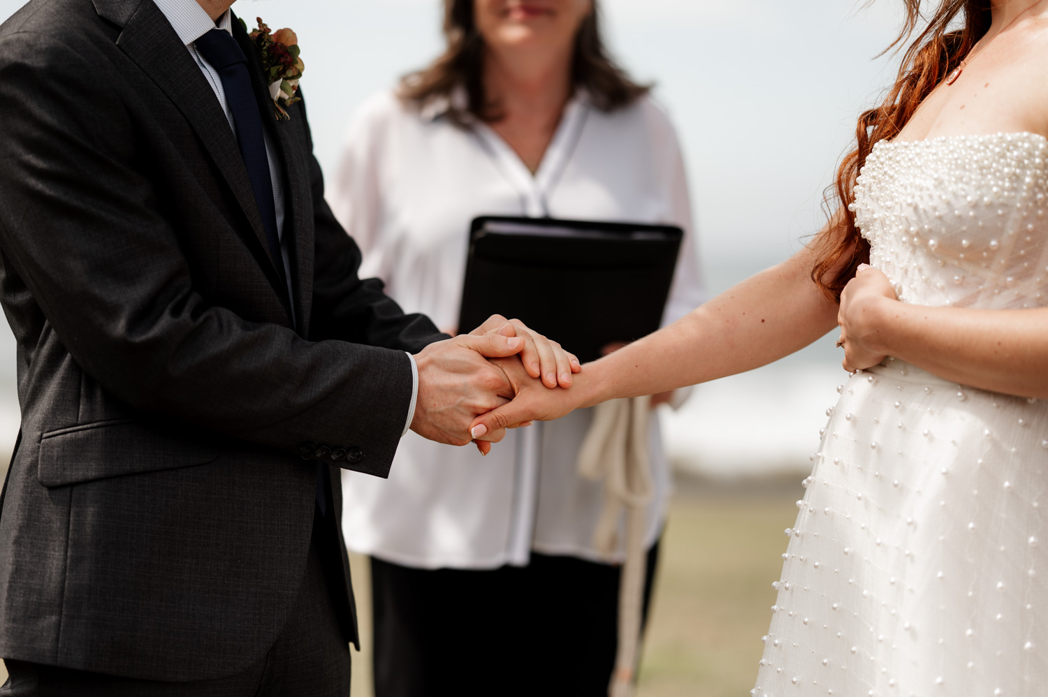 A couple exchanging vows and holding hands during an outdoor wedding ceremony at the Yachats Inn, with an officiant standing in the background.