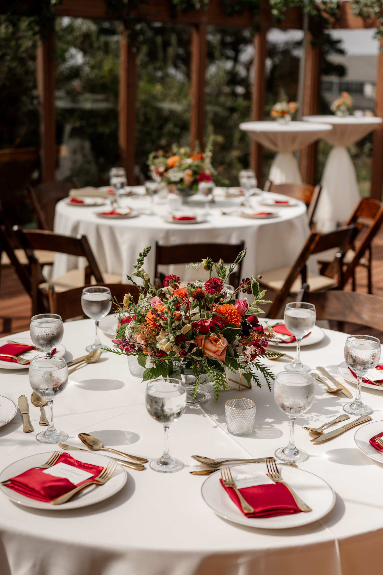 A beautifully arranged table featuring a white tablecloth, a vibrant floral centerpiece, neatly folded red napkins, and an array of glassware in a room filled with natural sunlight at the Yachats Inn.