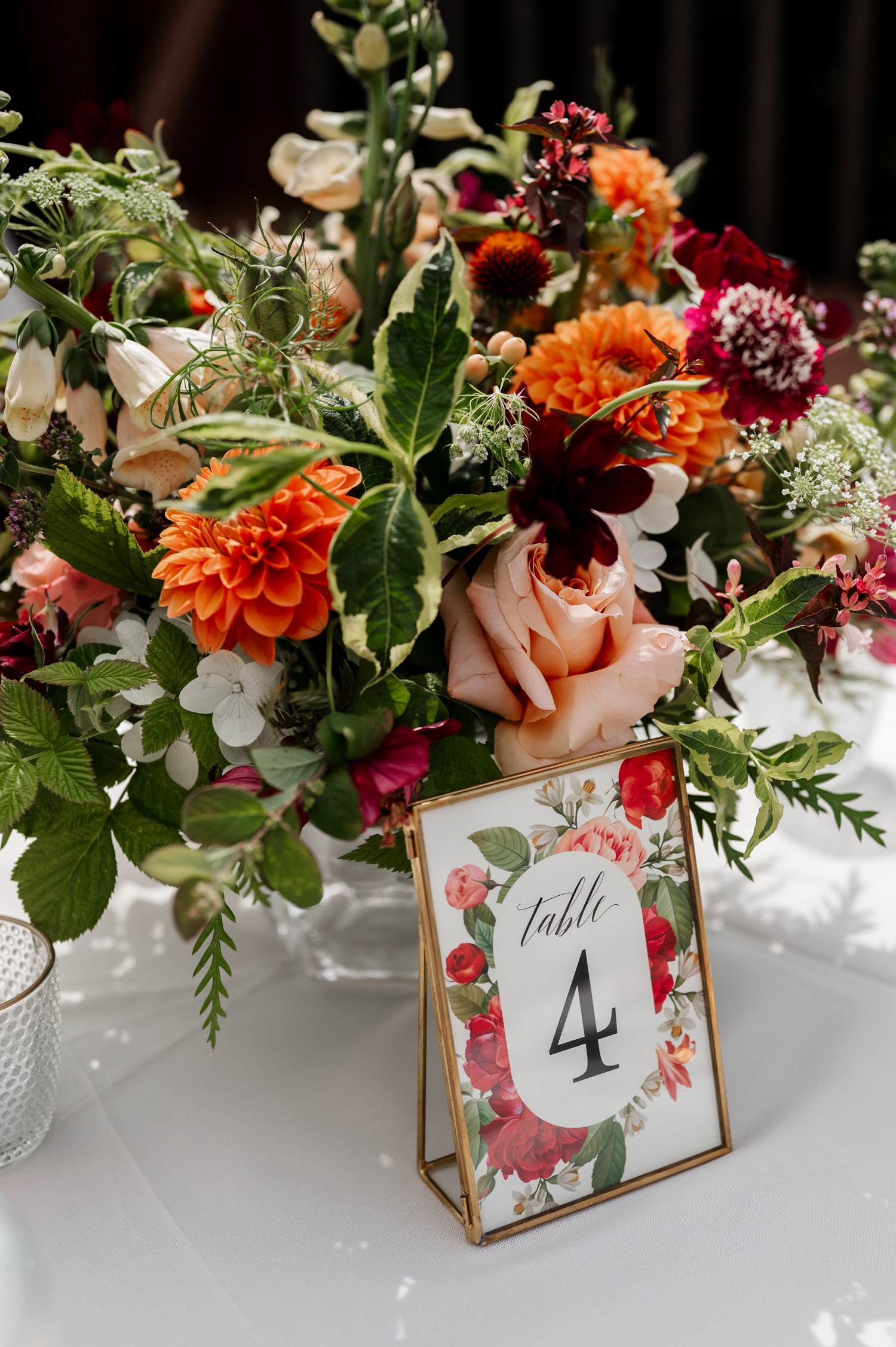 A vibrant floral centerpiece showcasing orange, pink, and red flowers with a Table 4 sign rests on a white tablecloth at the Yachats Inn wedding.