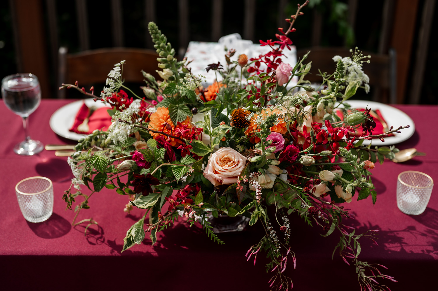 A vibrant floral centerpiece on a burgundy tablecloth at the Yachats Inn, surrounded by glassware and plates with red napkins.