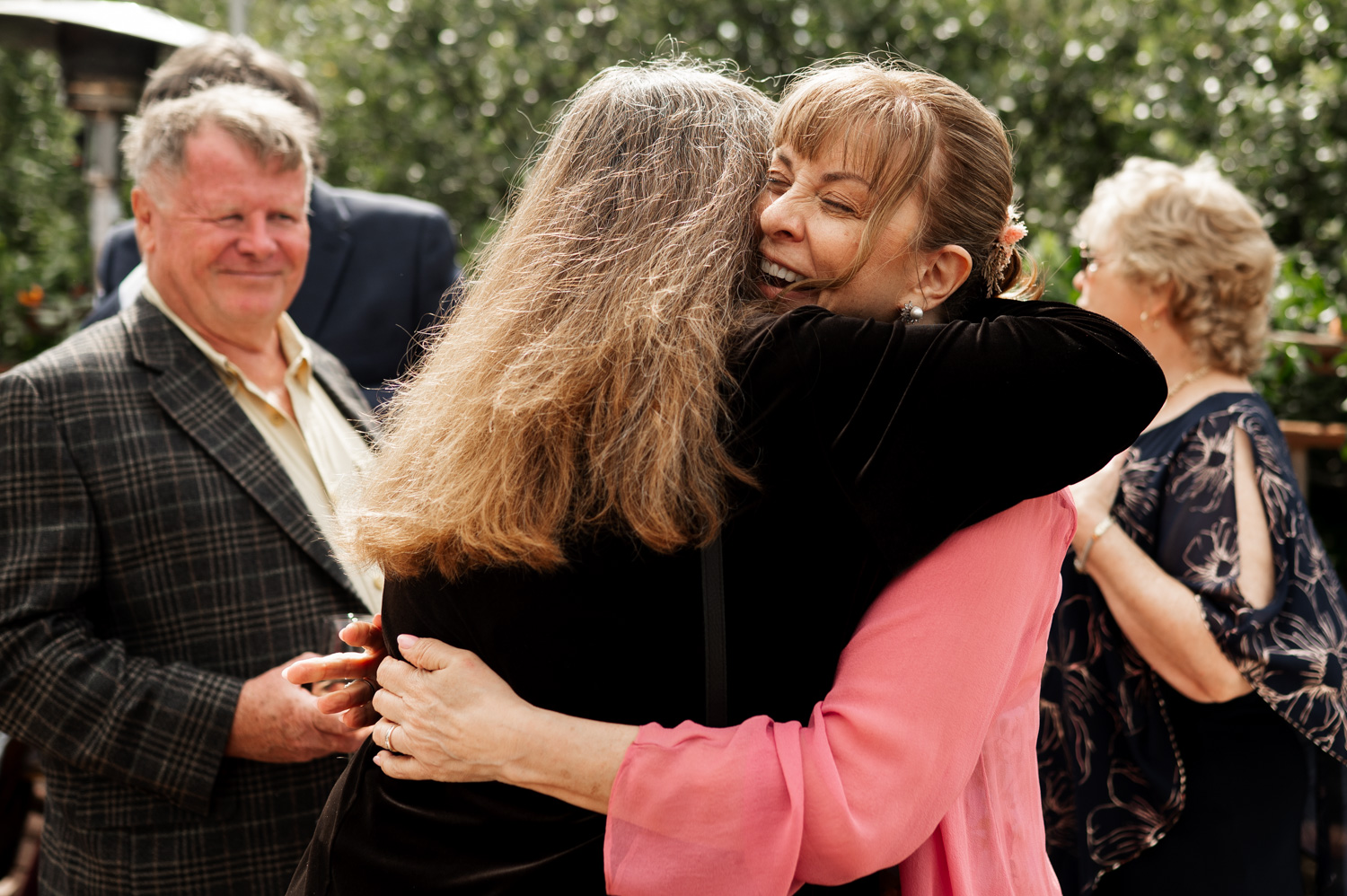 Two women embracing at an outdoor gathering, with smiling onlookers in the background, captured in wedding photos at the Yachats Inn.