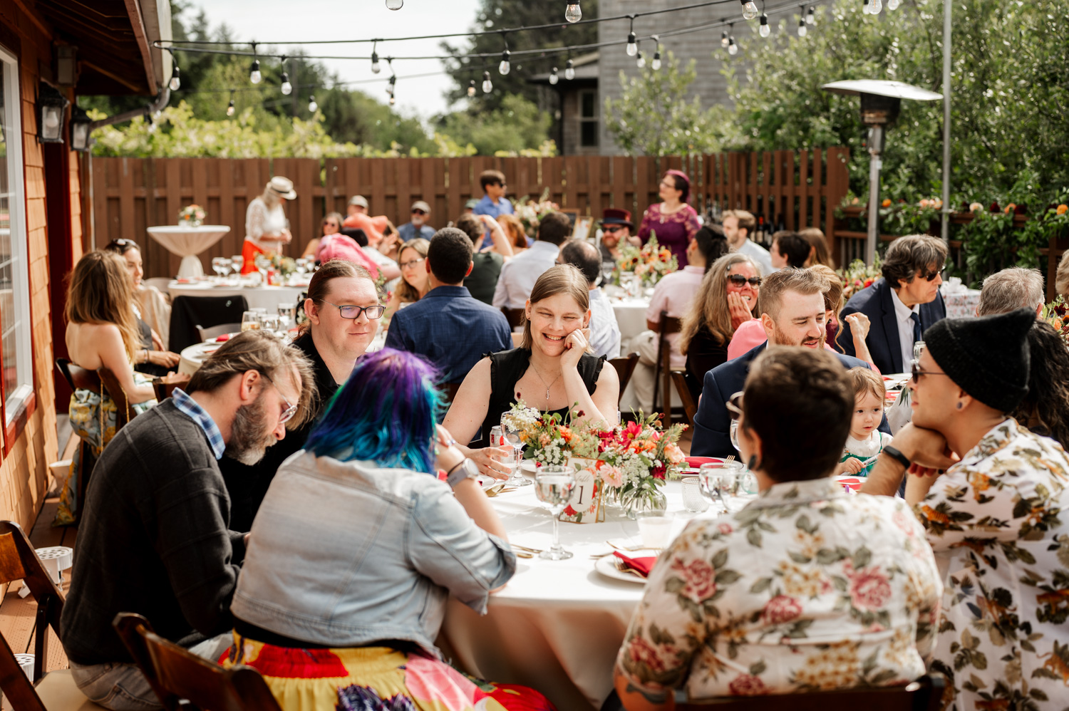 People enjoying an outdoor gathering with tables filled with food and decorations under string lights at Yachats Inn.