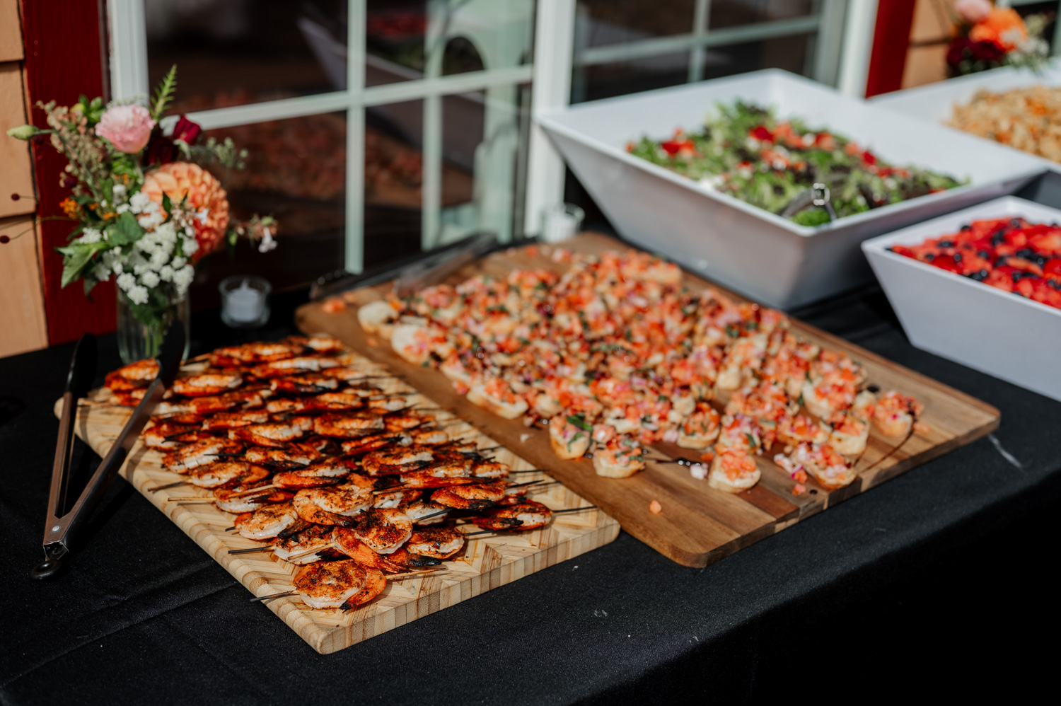 A variety of appetizers arranged on a table with fresh flowers and colorful salads in white bowls, conveying a sense of elegance typical of wedding settings at the Yachats Inn.
