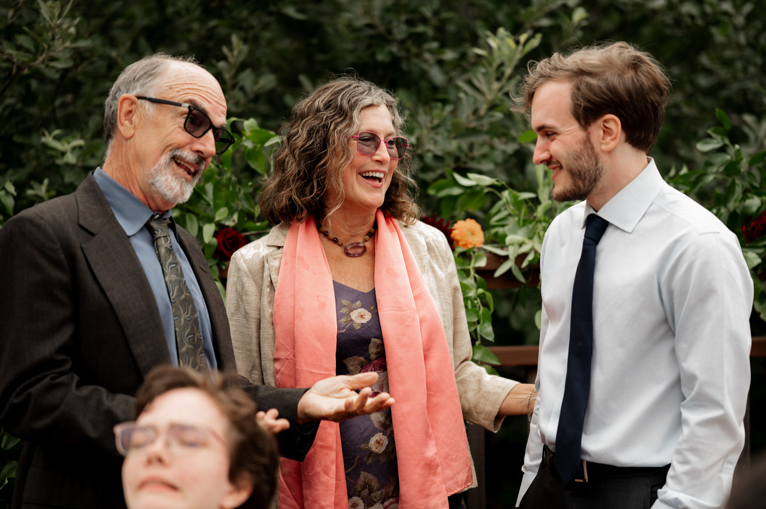 Three people happily converse outdoors, surrounded by vibrant flowers and lush greenery at the Yachats Inn.