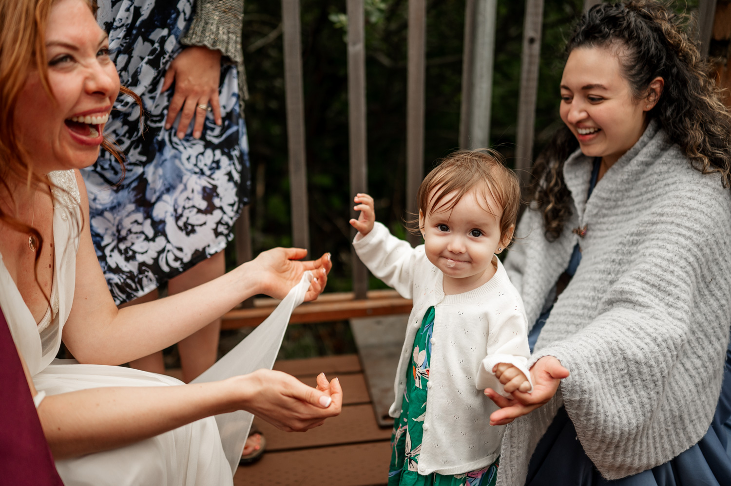 Adults and a smiling toddler gather outdoors, capturing a joyful moment at the Yachats Inn with nature providing a stunning backdrop.