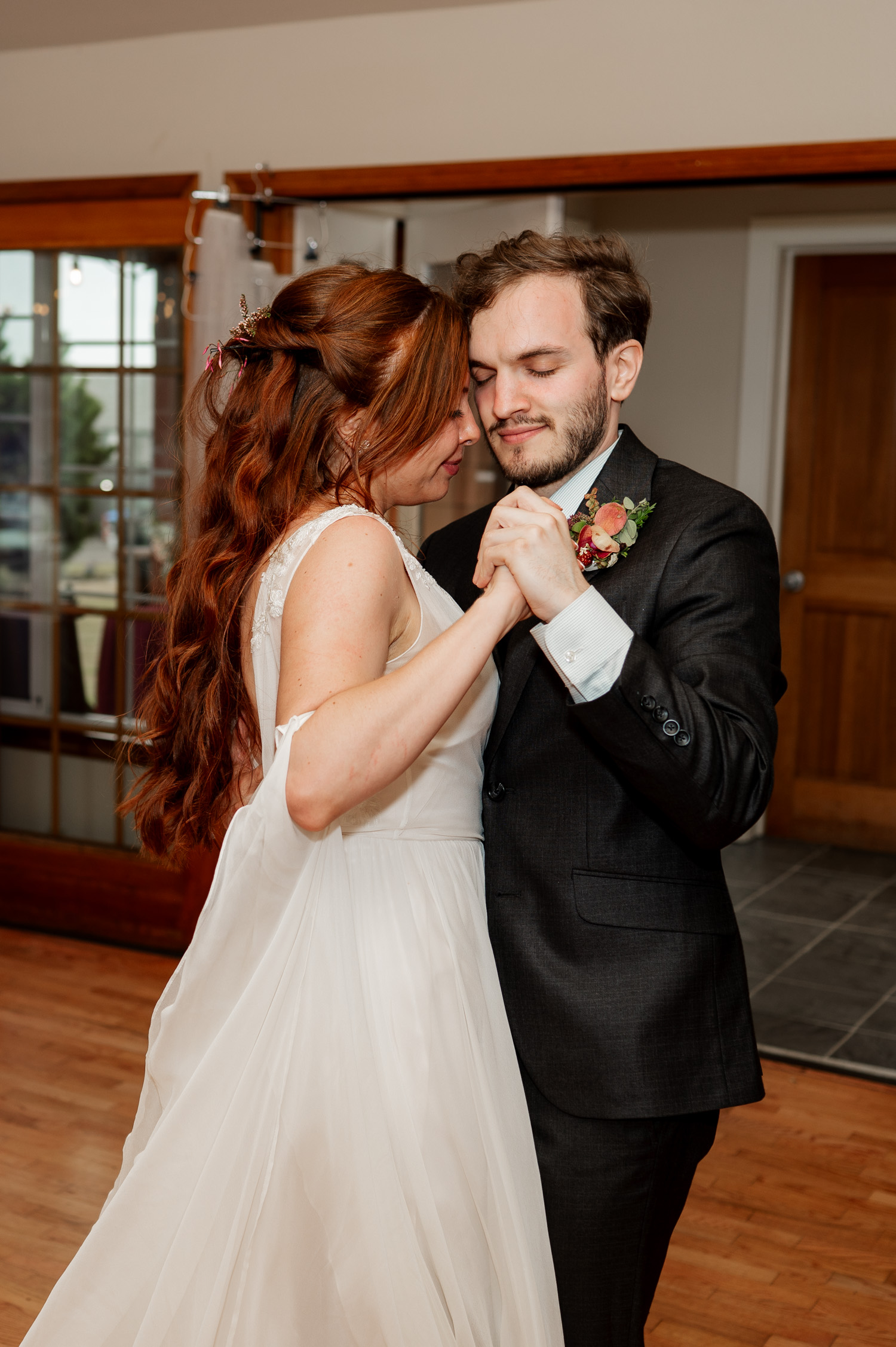 A couple in wedding attire shares a tender dance indoors at the Yachats Inn, smiling softly with closed eyes.