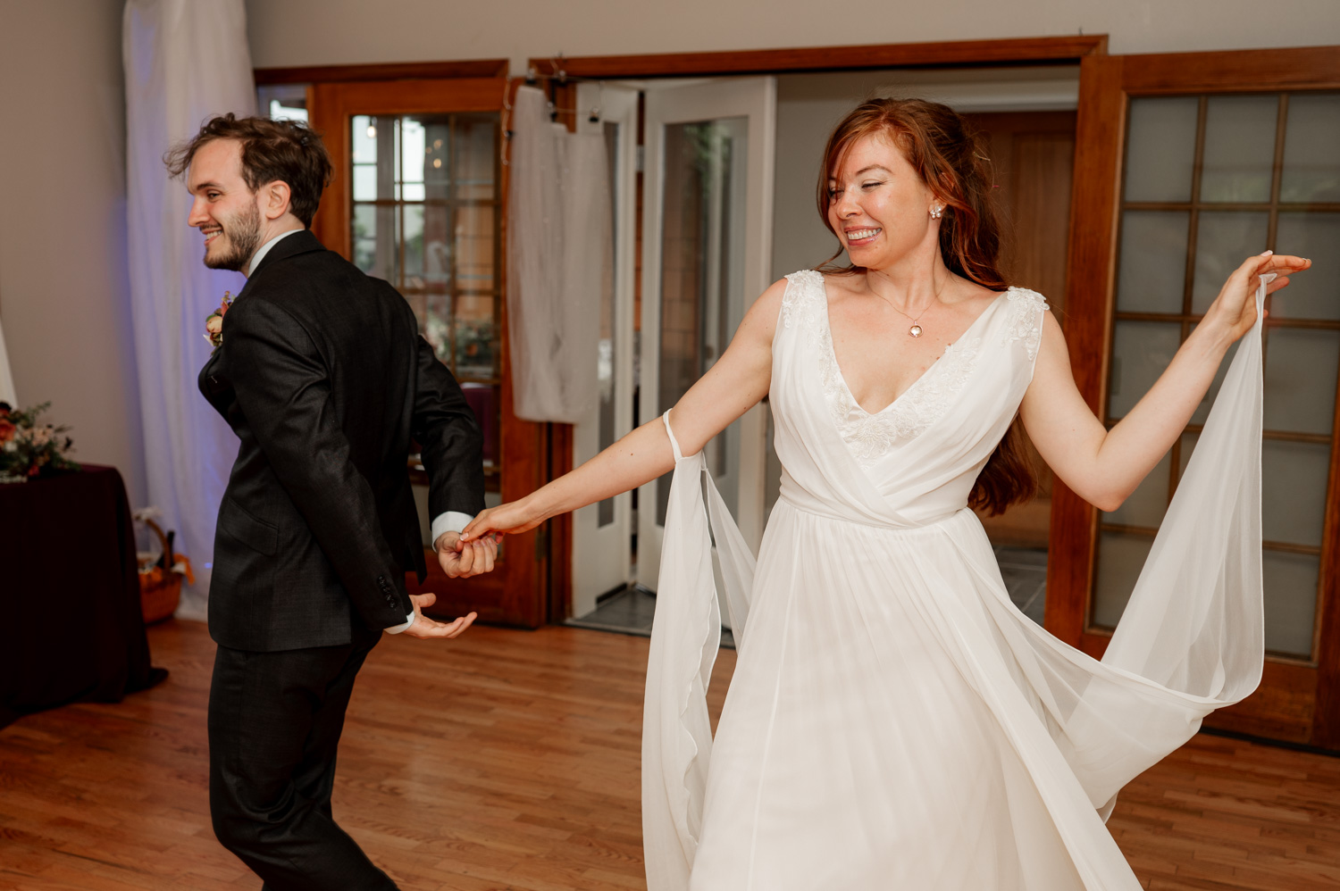 A bride and groom dance on a wooden floor at the Yachats Inn, holding hands as the bride twirls her dress.