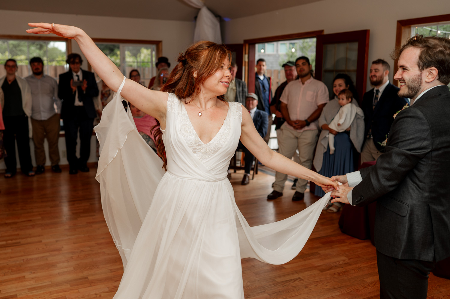 A bride and groom dance joyfully in a room at the Yachats Inn as guests watch and take candid photos of the celebration.
