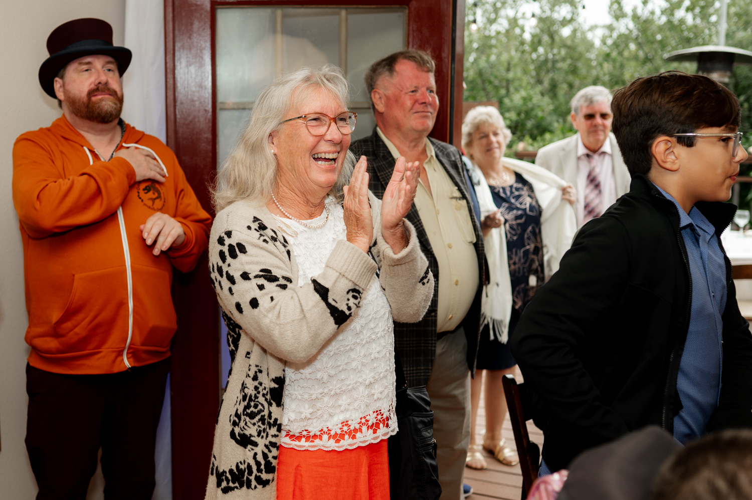 A group of people smiling and clapping indoors at the Yachats Inn, including a woman wearing a white and black sweater.
