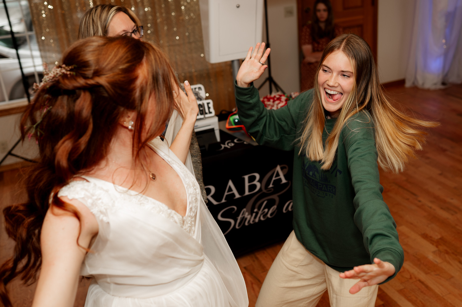 A bride and guest dancing together with joyful expressions at an indoor wedding reception.