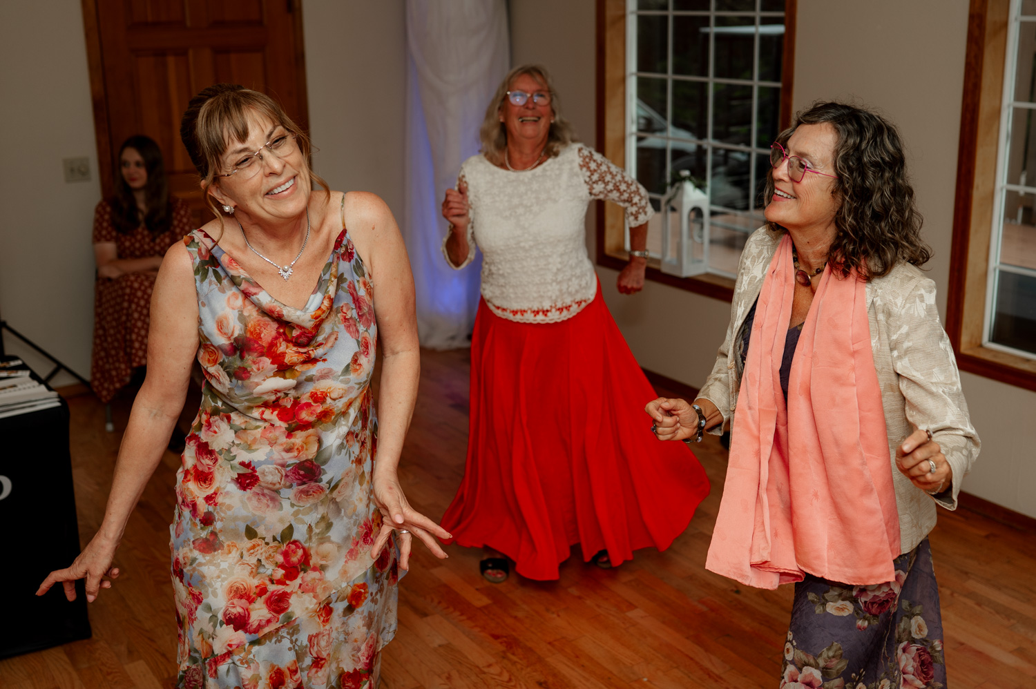 Three women joyfully dance on wooden floors, their colorful dresses and scarves swirling around them like a vibrant celebration.