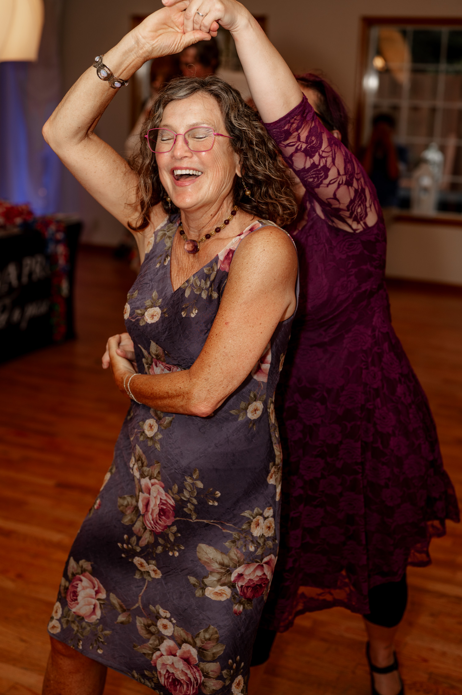 Two women joyfully dancing together at an indoor event, smiling and twirling.