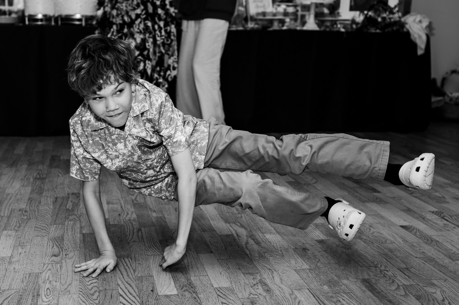 A child performs a one-handed breakdance move indoors, with legs outstretched, surrounded by wedding photos at the Yachats Inn.