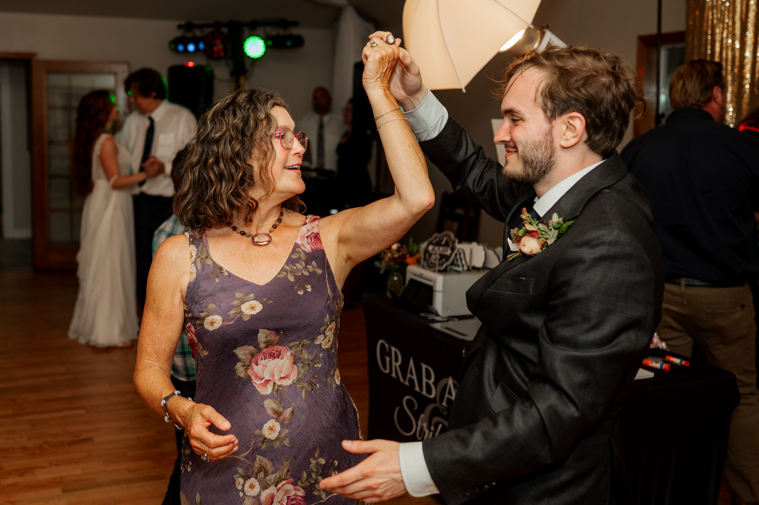 A woman in a floral dress dances joyfully with a man in a suit during a wedding celebration at the Yachats Inn.